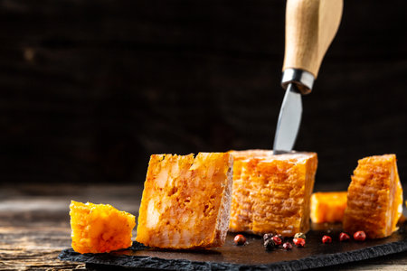 Cheese piece of Spanish manchego cheese made from cow milk with red paprika close up. cheese farmer. The concept of natural eco dairy products, Craft cheese from cows and goats milk.の写真素材