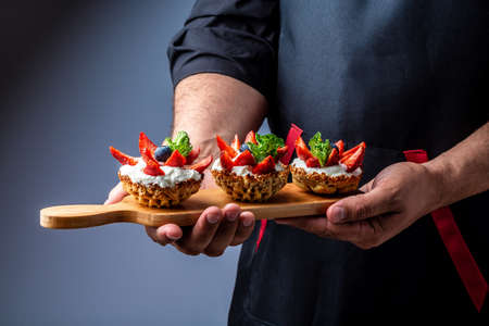 Fruit dessert tarts with cream, strawberry and blueberry in the hands of the chef. banner menu recipe place for textの写真素材