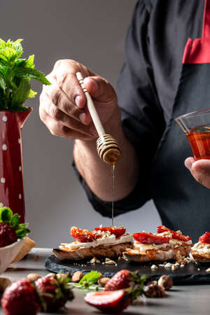 chef sprinkle the honey sweet sandwiches with strawberries, cheese, camembert, brie, nuts and honey on the whole grain bread bruschetta cooking by chef handの写真素材