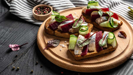 Herring fillet. Sandwich with salted herring, slice beetroot, green cucumber, onion and microgreen on the toasts. Scandinavian cuisine. Tradition Danish open sandwich. top view.の写真素材