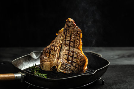 Grilling a tasty tender marinated t-bone steak seasoned with fresh rosemary on frying grill pan on black. wagyu porterhouse grilled beef steak. banner, menu, recipe, place for text.の写真素材