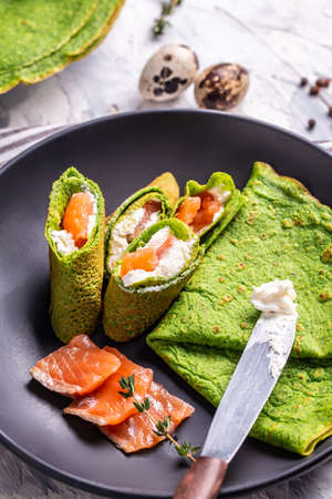 Green pancakes or crepes from spinach Served with salted salmon and soft cheese. trendy vegetarian food. vertical image.の写真素材