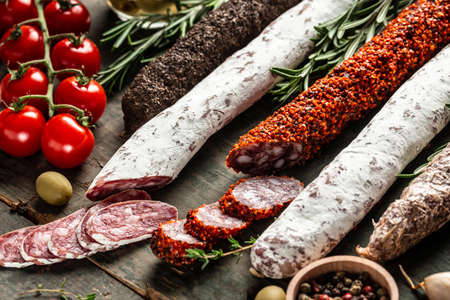 Variety of dry cured chorizo, fuet and other sausages cut in slices with herbs on wooden background....