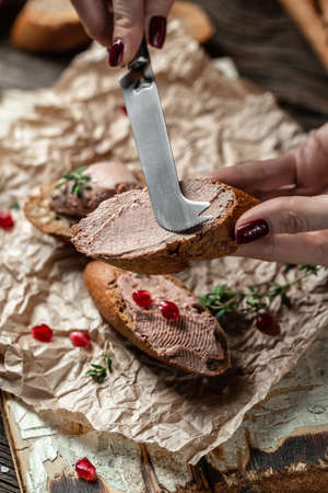 Close up Woman hands preparing and eating gourmet Belgian duck liver pate bread. Fresh homemade chicken liver pate on toasted bread with greens and pomegranate. vertical image.の写真素材
