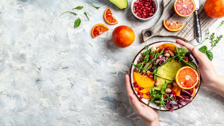 Girl holding vegan, detox Buddha bowl with avocado, persimmon, blood orange, nuts, spinach, arugula and pomegranate, balanced food. space for text. top view.の写真素材