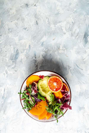 Healthy vegan lunch Buddha bowl avocado, persimmon, blood orange, nuts, spinach, arugula and pomegranate. Healthy balanced eating. top view. vertical image.の写真素材