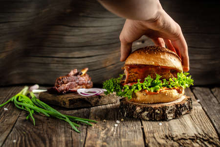 hands holding home made tasty burgers with grilled pork ribs on the wooden table. american food concept. fast food meal. banner, menu, recipe, place for text.の写真素材