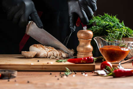 The chef in black gloves cuts with knife the chicken fillet on the kitchen, Restaurant menu, dieting, cookbook recipeの写真素材