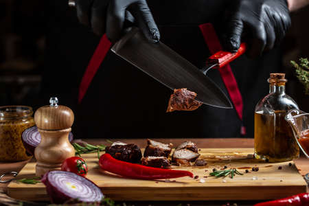 The chef in black gloves cuts with knife the beef fillet on the kitchen, Restaurant menu, dieting, cookbook recipe.の写真素材