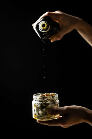 Cheesemaker showing the proceeding to make cheese , Chef hands adding olive oil in Jar with cheese marinated in oil on white wooden table. Ecology and eco-products.の写真素材