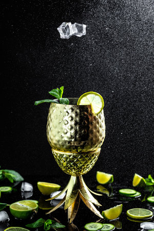 Ice falling into copper mug for a Moscow Mule cocktail splashing in copper cup with lime, blood orange, ginger beer, vodka and mint, freeze motion.の写真素材