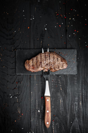 Steak on fork on dark wooden background. banner, menu recipe place for text, top view vertical image.の写真素材