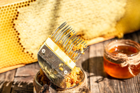 Jar of fresh honey with assorted tools for beekeeping, a wooden dispenser and tray of honeycomb from a bee hive in a still life on a wooden table outdoors with copy space.の写真素材