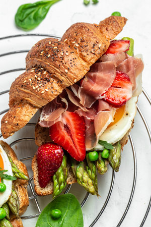 Breakfast, business lunch, sandwiches croissants with avocado, asparagus, jamon, ham, prosciutto, strawberries sunny side up eggs. Food recipe background. close up.の写真素材