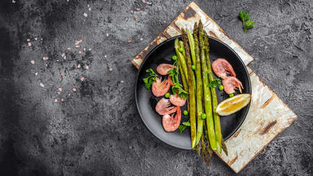 Delicious baked asparagus, shrimps, green peas and lemon on black background. Keto paleo lunch, top view,の写真素材