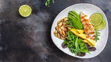 Healthy buddha bowl lunch with grilled chicken, halloumi, avocado, green rocket salad, lime, sesame and seeds. banner, menu recipe place for text, top view.の写真素材