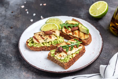 Grilled halloumi sandwich with avocado guacamole, arugula. Toast with grilled cheese and avocado. Health food.の写真素材
