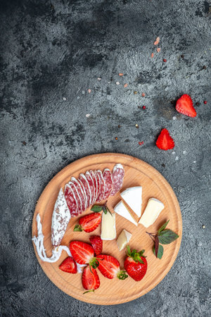 Traditional Spanish Fuet thin dried sausage with Camembert cheese, strawberries and glass rose wine on dark background. vertical image. top view.の写真素材