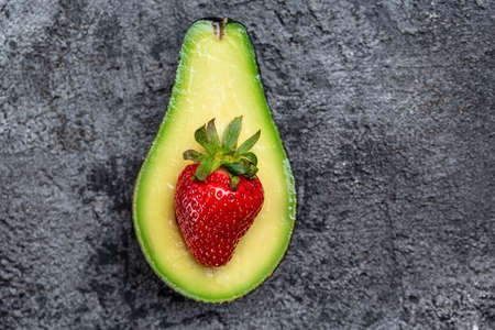 Avocado cut half and slice with strawberry on dark background. Detox concept. Long banner format....