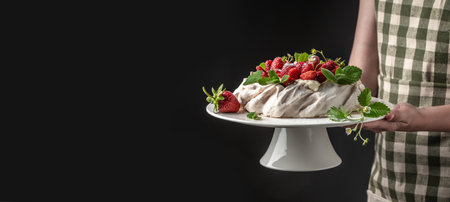 delicious homemade pavlova cake with fresh strawberries and whipped cream. Female baker decorating delicious meringue cake, Long banner format.の写真素材