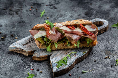 Fresh submarine sandwich with prosciutto ham, sun-dried tomatoes, gherkins, parmesan and arugula. banner, menu, recipe place for text, top view.の写真素材