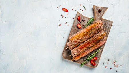 raw Lula kebab on skewers with spices on a cutting board light background. Lula kebab, traditional Caucasian dish. Long banner format. top view.の写真素材