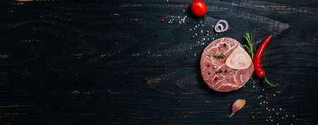 fresh meat. italian ossobuco steak on the bone with rosemary and spices on black stone background. Long banner format. top view.の写真素材