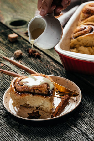 Cinnabon. Woman's hand spreading vanilla icing freshly baked cinnamon rolls, vertical image. top view. place for text.の写真素材