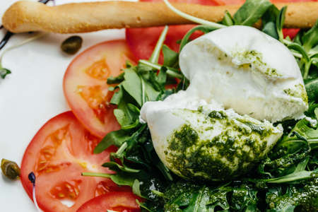 Salad with traditional italian burrata cheese with arugula, tomatoes and green pesto, Food recipe background. close up.の写真素材
