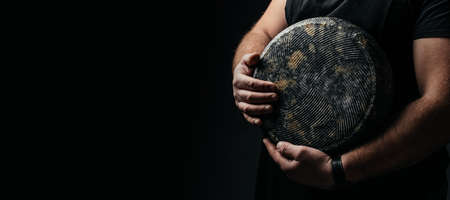 craftsmanship hands have a typical Italian cheese. French tomme cheese in the hands of a cheesemaker on dark background. Long banner format.の写真素材