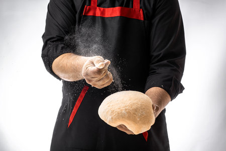 White flour flying into the air as pastry chef in white suit slams ball dough on white powder...
