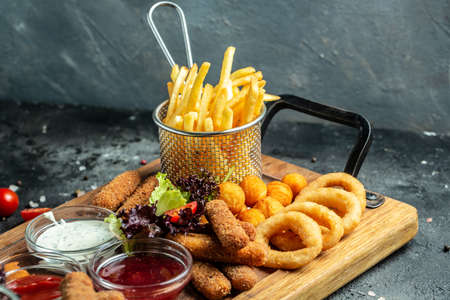 take away food mozzarella sticks, onion rings, french fries, chicken nuggets and sauce on a wooden board. banner, menu, recipe place for text.の写真素材
