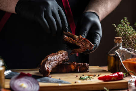 The chef in black gloves Grilled pork ribs on the kitchen. american food concept. fast food meal. banner, menu, recipe, place for text.の写真素材