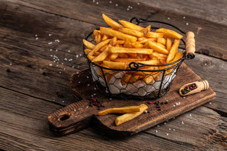 Fresh hot french fries with salt and spices on cutting board on wooden table background, unhealthy calories meal,の写真素材