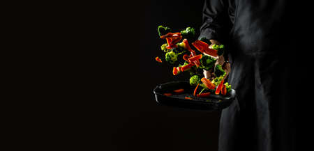 Professional Chef Cooks Flambe Style. Hands of cook frying vegetables on pan. flying vegetables scattering in a freeze motion,の写真素材