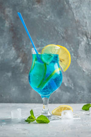 blue cold drink and ice cubes, with fresh green mint leaves on deep blue and light blue background. Alcoholic or non-alcoholic cold longdrink.の写真素材