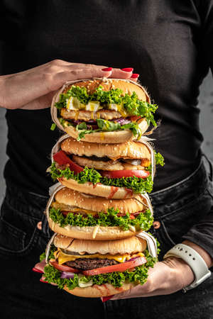 Young girl holding in female hands fast food burger, american unhealthy calories meal on background, mockup with copy space for text message or design, hungry human with grilled hamburger front view.の写真素材