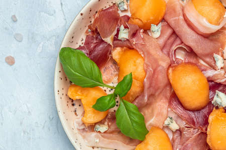 Summer appetizer with sweet melon and prosciutto and basil. Antipasti, Traditional Spanish and Italian appetizer. Top view on white stone table, Long banner format. top view,の写真素材
