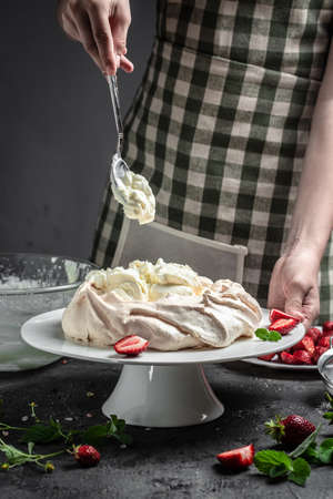 delicious homemade pavlova cake with fresh strawberries and whipped cream. Female baker decorating delicious meringue cake, vertical image. top view. place for text,の写真素材