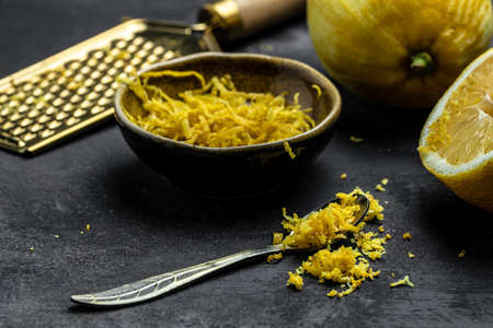 Peeling lemon rind to add zest to Mediterranean recipes. Grater peel and lemon zest on black background, place for text, top view.の写真素材