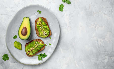 Healthy avocado toasts for breakfast or lunch with rye bread, sliced avocado, pumpkin seeds, salt...