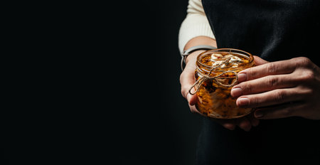 Female hands holding glass jar with cheese in olive oil and aromatic herbs on a dark background. banner, menu, recipe place for text.の写真素材