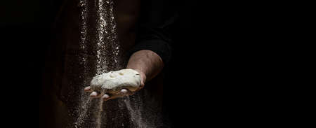 flying pizza dough with flour scattering in a freeze motion of a cloud of flour midair on black. Cook hands kneading dough. copyspace.の写真素材