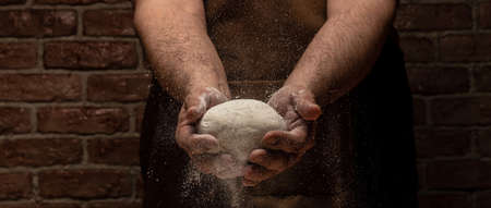 Beautiful and strong men's hands knead the dough from which they will then make bread, pasta or pizza. A cloud of flour flies around like dust. food conceptの写真素材