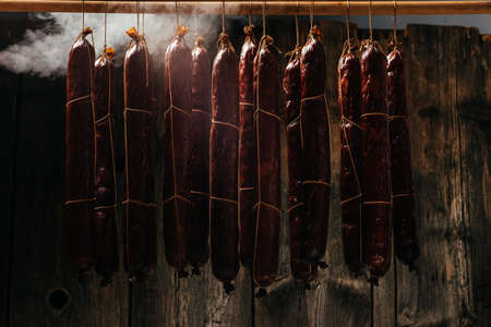 Process of smoking sausage hang in a cupboard with smoke. Clouds of smoke rise up and envelop the sausages hanging in a row.の写真素材