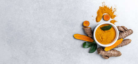 turmeric powder in spoon with turmeric root. curcuma or curcumin on concrete background. Spice, natural coloring, alternative medicine. Long banner format. top view.の写真素材