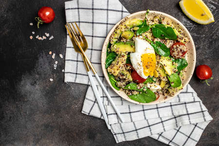 Keto diet plate quinoa, avocado, egg, tomatoes, spinach and sunflower seeds on dark background....