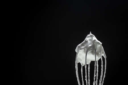 Metal whisk for whipping eggs with cream white raw meringue for perfect peaks isolated on black. Whipped cream, cookie recipe.の写真素材