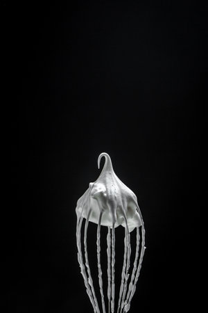 Metal whisk for whipping eggs with cream white raw meringue for perfect peaks isolated on black. Whipped cream, cookie recipe. vertical image. place for text.の写真素材
