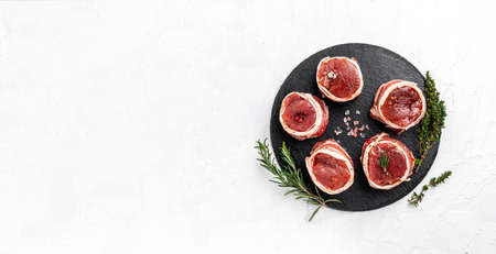 Raw beef filet Mignon steak on metel tray with pepper and salt, filet mignon. beef tenderloin steaks wrapped in bacon and thyme on light background. Long banner format. top view.の写真素材